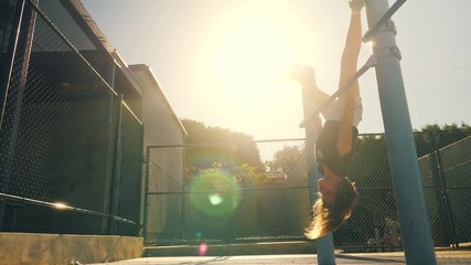 Active 8 year old school girl exercising upside down in school yard outdoors. Slow motion, 4K UHD. 