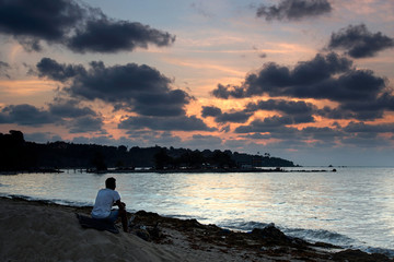 A man is sitting on a dirty beach with twilight sky in background