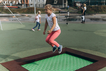 Obraz premium Cheerful adorable girl jumping outdoors in kindergarten.Happiness, sport, leisure, childhood, healthy concept