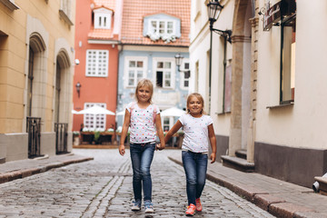 Fototapeta na wymiar Cheerful happy girl travel together, hugging, holding hands and laughing outdoors in old town. Childhood, tourism, positive concept
