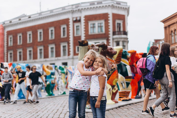 Obraz premium Little adorable cute girls in the street walking together hgging and holding hands and smiling. Urban, vacation, travel, childhood concept