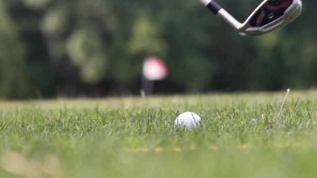 Close up of a moment when ball being hitted by a wedge on the green golf pitch on a sunny summer day rising grass up. Outside. slow motion
