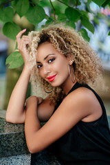 Fashionable young beautiful african american woman with afro hairstyle sitting in park