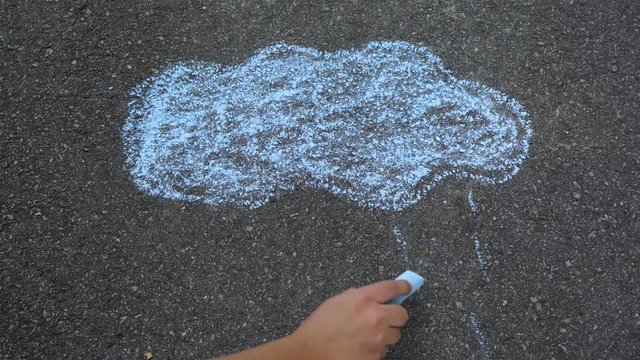 Childs hand drawing rainy blue cloud and raindrops falling down on pavement. Chalk drawing. Real tim e 4k video footage.