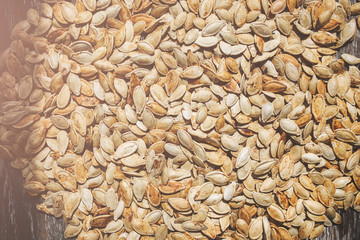 Fried pumpkin seeds lying on the old rustic background. Vegetarian superfood. Healthy diet. Natural texture background. Vertical photo.