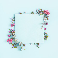 Flowers composition. Paper blank, pink flowers on pastel blue background. Flat lay, top view, copy...