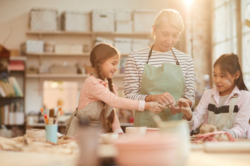 Waist up portrait of art teacher working with kids in pottery class scene lit by sunlight, copy space