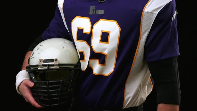 American football player holding a head gear against black background