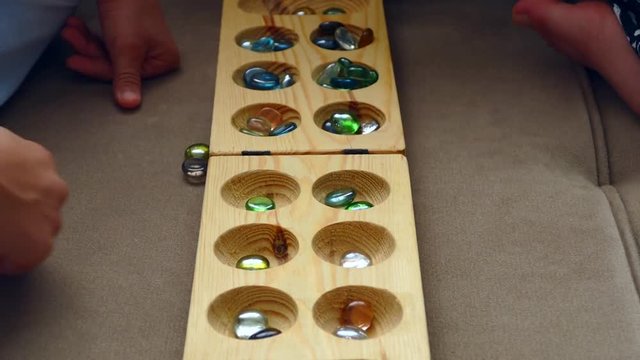Traditional Mancala boardgame with glass pieces on marble table