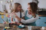 Smiling mom and daughter coloring eggs at home