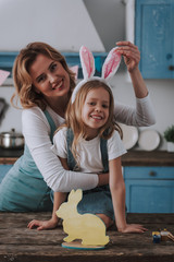Happy mom holding rabbit ear on head of daughter