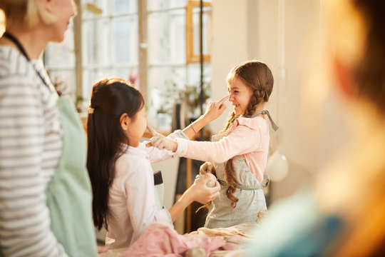 Portrait of two cute girls having fun during pottery workshop in art class, copy space