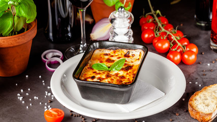 The concept of Italian cuisine. Baked lasagna in a black ceramic baking dish. The chef decorates the dish in the restaurant when serving. Background image. copy space