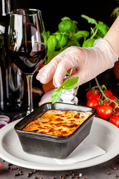 The concept of Italian cuisine. Baked lasagna in a black ceramic baking dish. The chef decorates the dish in the restaurant when serving. Background image. copy space