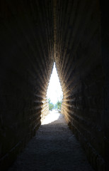 Obraz premium Path through a dark narrow tunnel in old stone ruins. Sunlight and green trees at the end of the tunnel