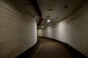 Path through a dark curved arched tunnel with light walls in an old abandoned building