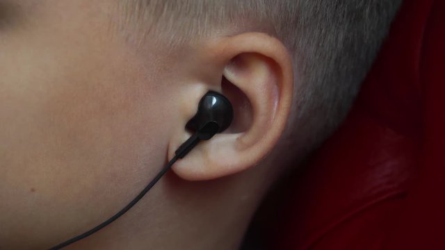 Closeup of young kid's ear with small black modern earphones in it. Real time 4k video footage.
