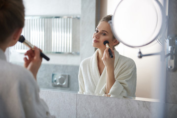 Young lady laying powder blusher on cheek