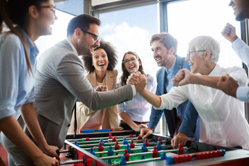 Business people having great time together.Colleagues playing table football in office. - obrazy, fototapety, plakaty