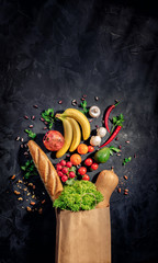 Healthy food in full paper bag of different products vegetables and fruits on dark background © Storm