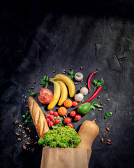 Healthy food in full paper bag of different products vegetables and fruits on dark background