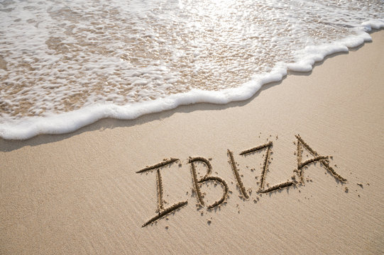 Simple Ibiza Spanish holiday getaway message written in smooth sand with an incoming wave on a tropical beach