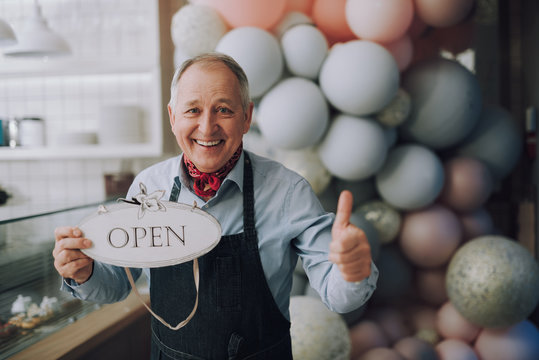Happy small business owner holding open sign and showing thumbs up