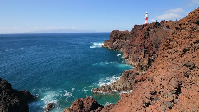 Panoramic view from the volcanic cliffs of the famous lighthouse of Teno in the Isle of Tenerife while some tourist are walking next to the lighthouse