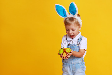 funny happy child boy with easter eggs and bunny ears on yellow