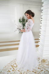 Elegant bride with a bouquet of blossoming sakura in her hands in a bright interior in full growth.