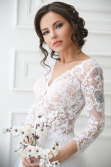 Portrait of a beautiful elegant bride with a bouquet of sakura in a bright interior.
