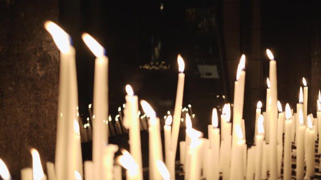 Candles burn inside and are reflected in window, purgatory or prayer candles in a church. 4k footage
