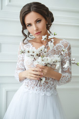 Portrait of a beautiful elegant bride with a bouquet of sakura in a bright interior.