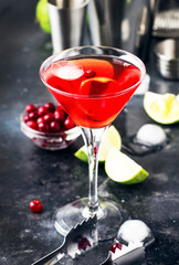 Classic alcoholic cocktail cosmopolitan with vodka, liqueur, cranberry juice, lime, ice and orange zest, gray bar counter background, bartender tols, space for text