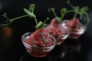 Red appetizing Tartar sauce in three pialas, decorated with a stem of sprouted green peas, close-up