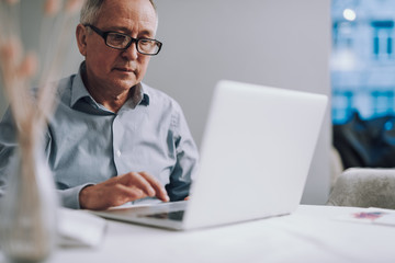 Old man in glasses using modern white laptop