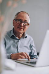 Good-looking old man in glasses using modern white laptop