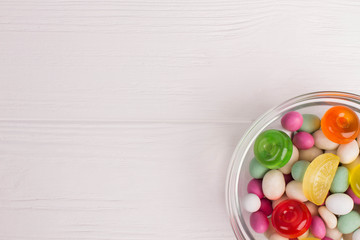 Multicolored bonbon sweets in glass bowl. Colorful candies on white wooden background with copy space.