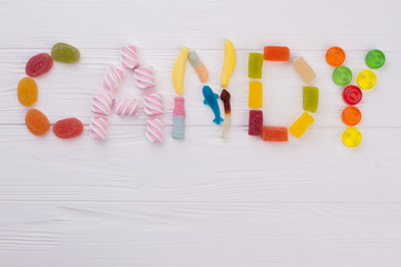 Colourful sweets spelling the word CANDY. Assorted colorful gummy candy letters spell the word CANDY on white wooden background.