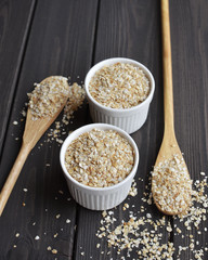 Rolled oats in bowls and spoons on dark wooden table background