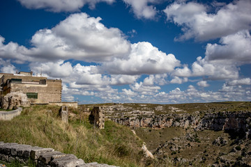 Fototapeta na wymiar Summer day scenery street view of the amazing ancient town of the Sassi with white puffy clouds moving on the Italian blue sky. Matera, Basilicata, Italy