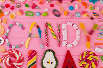 Mixed candies on color background. Composition from assorted sweets on pink wooden background. Yummy holiday treats.