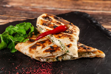 The concept of Georgian cuisine. Baked pita with suluguni cheese and cilantro. Serving dishes on a black stone slate. On a wooden background. copy space
