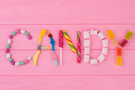 Word CANDY made of colorful candies. Various colorful candies arrange as a word CANDY on pink wooden background.