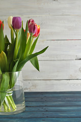 A colorful bouquet of tulips in a glass vase on a blue-white wooden background