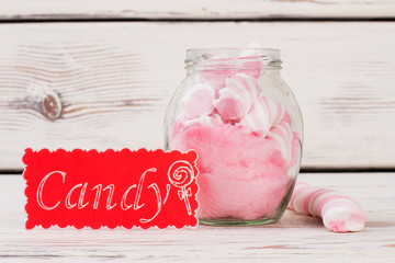Composition with sweets on wooden background. Pink marshmallows in glass jar and red card with inscription Candy.