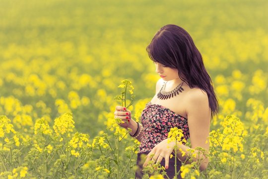 Beautiful woman in sunny summer love looking at rapeseed flower. Attractive young beauty girl enjoying the warm sunny sun in nature rapeseed field takes time feeling sustainability and contemplation