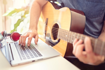 Musician playing acoustic guitar and recording music on computer
