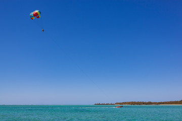 Parasailing in clear blue sky above the turquoise water near tropical island Mauritius