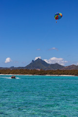 Parasailing in clear blue sky above the turquoise water near tropical island Mauritius